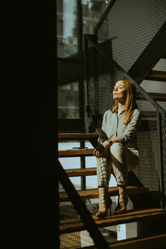 Woman sits on stairs with sunlight streaming through a window in a modern building
