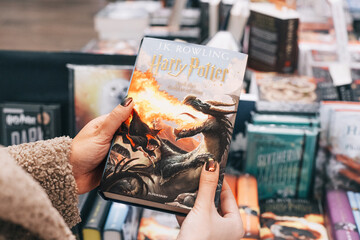 Naklejka premium 29 December 2024, Belgrade, Serbia: Person's hands browsing J.K. Rowling's Harry Potter and the Goblet of Fire book in a bookstore, featuring a dragon on the cover