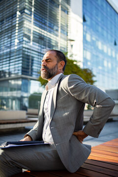 Businessman holding lower back in pain outside office