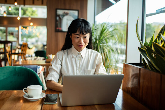 Woman working on laptop at cafe by window