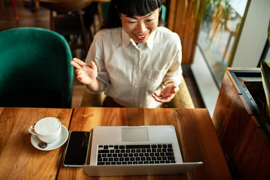Smiling woman video calling on laptop in cozy cafe