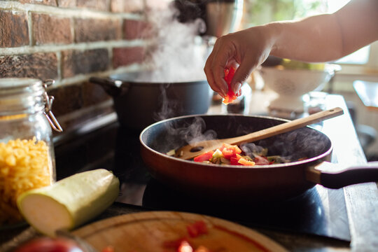 Hand adding peppers to steaming vegetables in a home kitchen