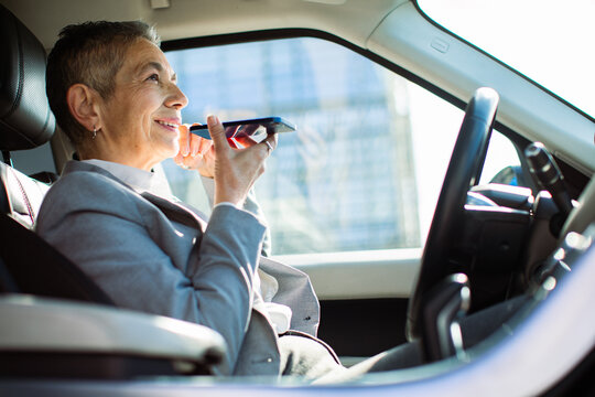 Smiling senior businesswoman using voice assistant in car