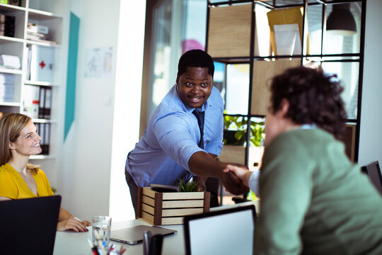 Colleagues greeting new hire with handshake in modern office