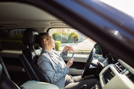 Mature driver applying lip balm with smartphone in a parked car