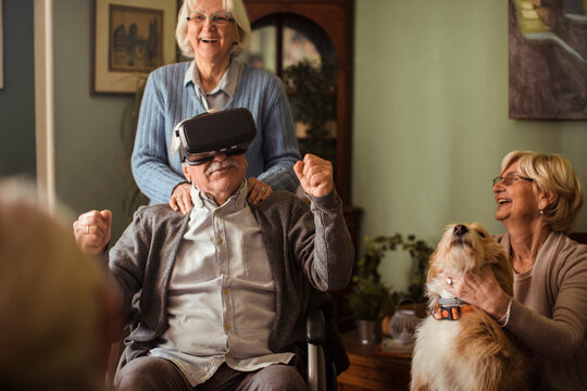 Senior man in wheelchair trying virtual reality at home with family and dog