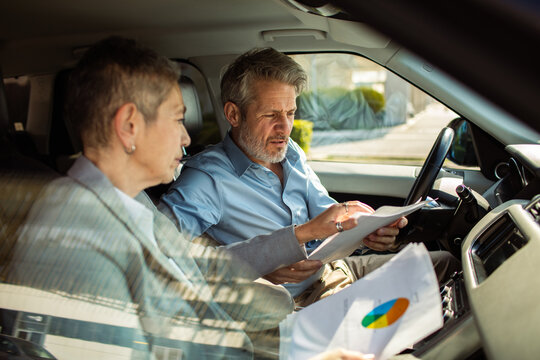Mature man and woman reviewing financial documents in a parked car