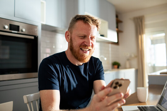 Smiling man using smartphone in home kitchen