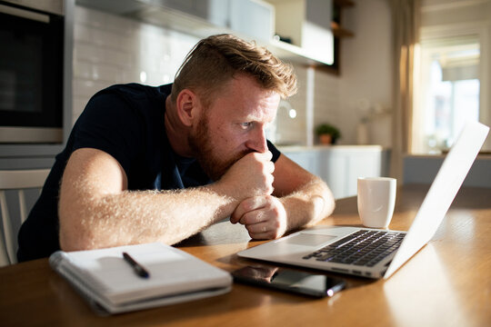 Worried man working on laptop at home kitchen