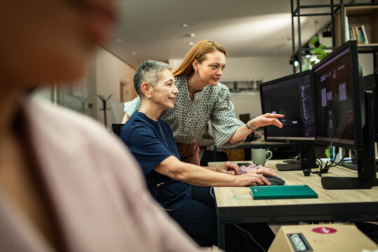 Two women collaborating on design software at dual monitors in modern office
