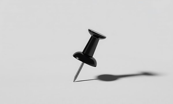 A single black push pin standing upright casting a shadow on a flat surface