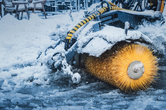 Snow sweeper brush actively clearing heavy snow and ice from a city street during cold winter weather