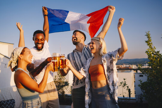 Diverse friends cheering and celebrating with french flag on rooftop