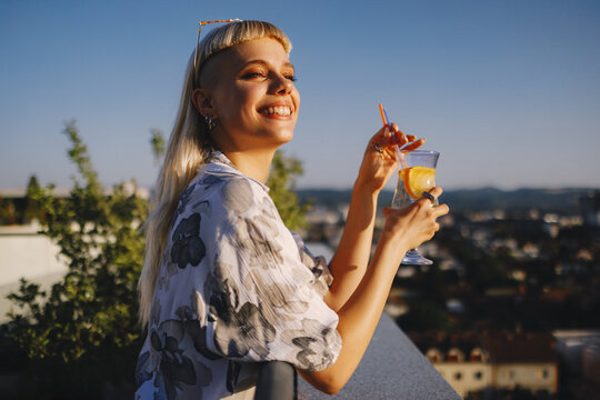 Happy woman enjoying drink on rooftop terrace at sunset