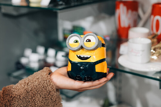 29 December 2024, Belgrade, Serbia: Person's hand holding a Minions character mug with large goggles, selecting merchandise in a gift shop