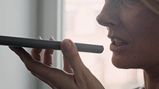 Close up of anonymous woman holding smartphone near face while recording voice message