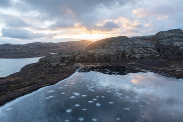 Fototapeta premium Stunning aerial view of a tundra lake covered in thin ice with distinct white circular patterns, reflecting the dramatic sunset sky in the Arctic