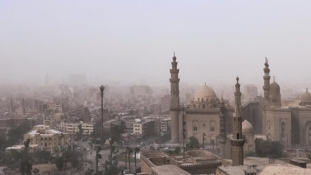 Two grand Cairo mosques with multiple minarets and imposing domes rise above the sprawling hazy cityscape of Egypt's capital, a symbol of Islamic heritage and history.