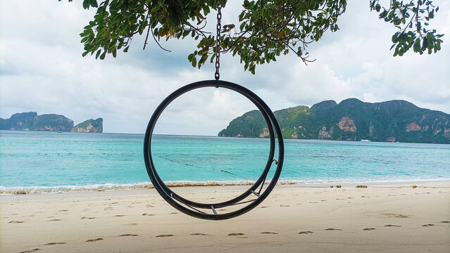 Phi Phi Island Thailand on August 15, 2026:  Empty circular swing hanging on tropical beach with turquoise sea and lush mountain background