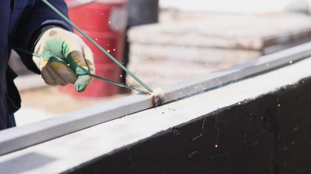 Worker Wearing Safety Gloves Meticulously Joining Steel Components During Construction. Precise Welding Of Steel Framework By Worker In Safety Gear At Residential Building Site