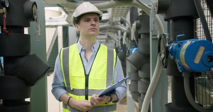 A male engineer conducts a routine inspection of an industrial HVAC system in a plant room, checking machinery for performance and safety compliance.