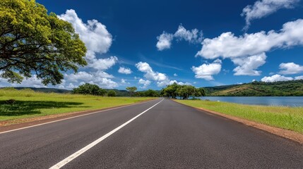 Fototapeta premium Highway stretches across the landscape with green grass and a lake visible in the background under a daytime sky