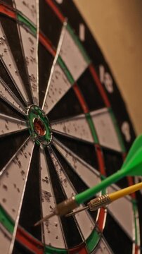 Vertical close up of colorful darts striking dartboard then hand of Black man retrieving them during relaxed game indoors