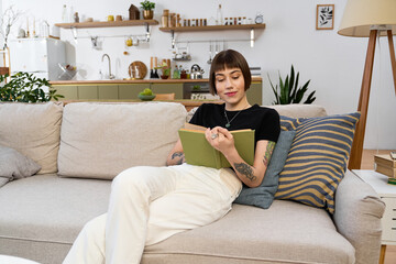 Obraz premium Young woman enjoys a cozy afternoon reading a book in her modern living room