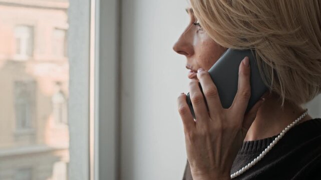 Close up of adult woman smiling lightly while speaking on smartphone during workday in modern office