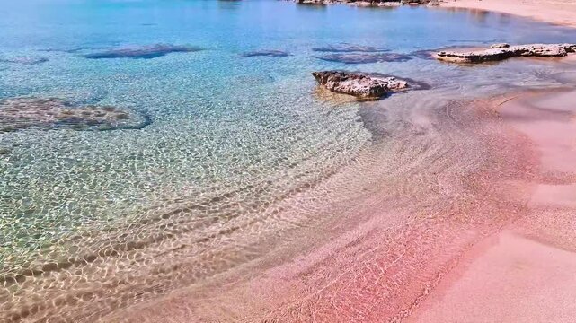 Empty exotic pink sand beach at Elafonisi, Crete. Transparent turquoise water with sea waves sound. Aerial perspective of deserted paradise shore in Greece, 4k high quality ground footage.