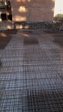 Vertical video. Detailed view of a steel rebar reinforcement grid laid out on a building foundation at a construction site, ready for pouring concrete to create a strong monolithic slab for a building