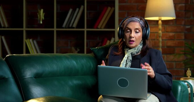 Indian asian senior businesswoman in corporate attire working on laptop at workstation in modern cozy office space experienced female executive with white hair sitting at professional desk area