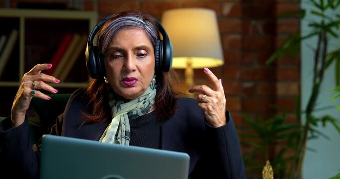 Indian asian senior businesswoman in corporate attire working on laptop at workstation in modern cozy office space experienced female executive with white hair sitting at professional desk area
