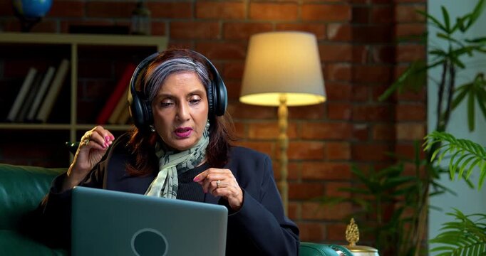 Indian asian senior businesswoman in corporate attire working on laptop at workstation in modern cozy office space experienced female executive with white hair sitting at professional desk area