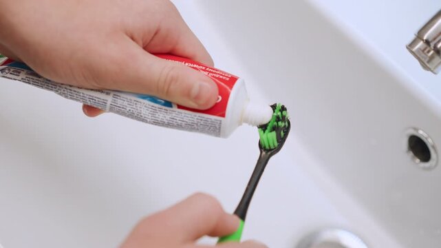 Gentle hands of grandma applying paste onto brush near sink calm bedtime routine careful measured squeeze green bristles white paste soft bathroom lighting warm caregiving moment comfort and support
