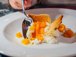 Close-up of a person tasting a deconstructed orange cheesecake with a silver spoon at a restaurant. © MalaikaCasal