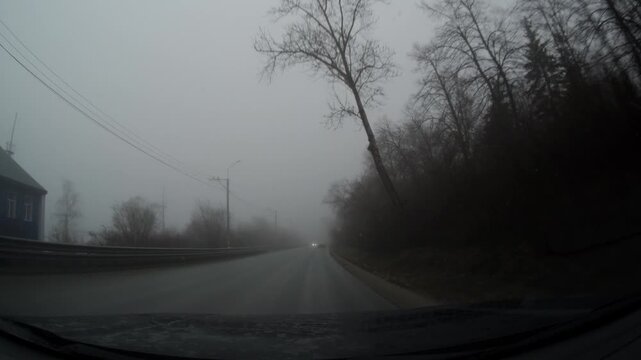 A car drives slowly along a foggy rural road. Driver point of View.