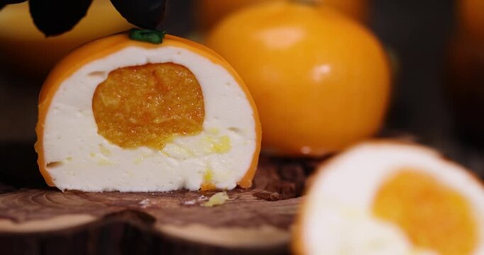 The cake is cut in half, a mousse cake with white cream and orange fruit filling in a glaze on a wooden split with clear details and organic texture in a macro