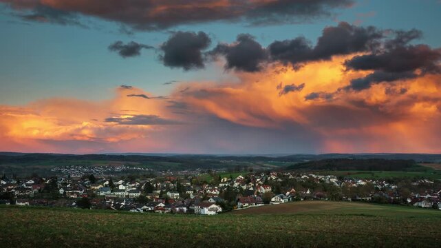 Time lapse of illuminated orange rain clouds over a scenic village. Dramatic sunset sky over rural landscape.