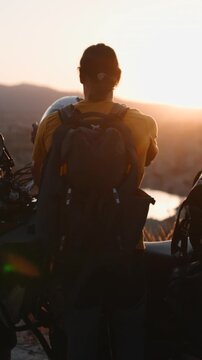 Biker with backpack putting on helmet watching a sunset over the mountains