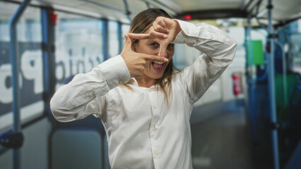 Obraz premium Woman framing a rectangle with fingers inside a bus interior on a street, wearing a white shirt and focusing on hands; playful focus.