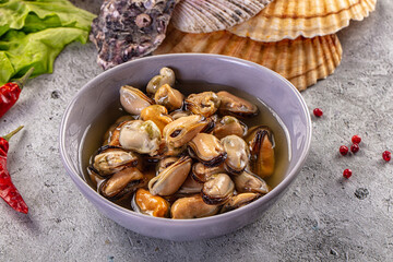 Fototapeta premium Marinated mussels in a bowl with chili peppers, lettuce, and seashells on a rustic grey background.