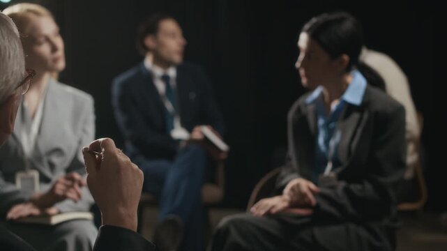 Rack focus shot of group of business people in formalwear with badges sitting on chairs in conference room and sharing ideas while attending business seminar