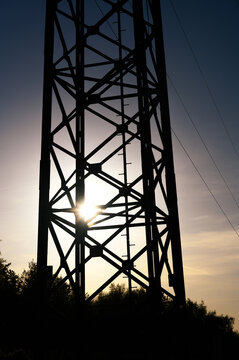 Silhouette of a tall metal pylon against a bright sunset sky