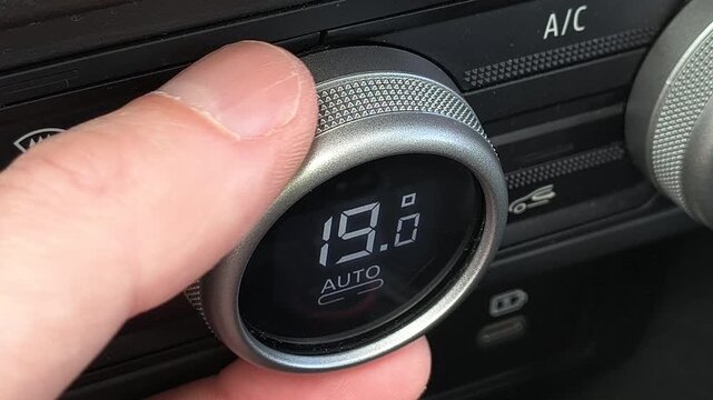Close up of hand adjusting car air conditioner temperature knob, decreasing degrees to seventeen in auto mode, modern vehicle climate control system, dashboard detail