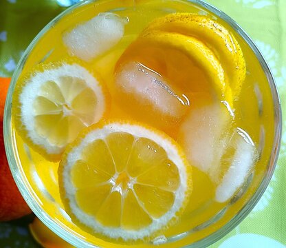 Lemon slices in orange juice with ice cubes in the glass fresh citrus fruit summer background