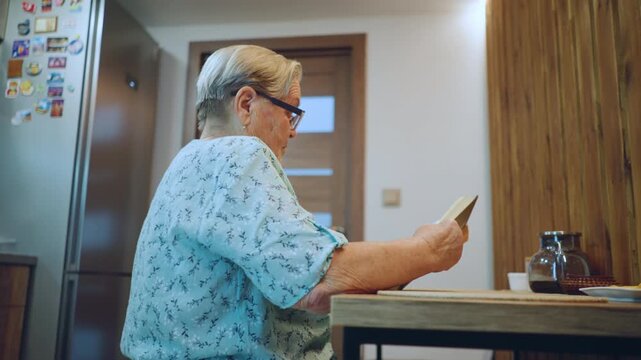 Senior lady enjoying peaceful moments. An elderly woman reflects on serene and sentimental kitchen scene. Senior woman quietly engages with cherished memories in her cozy kitchen setting