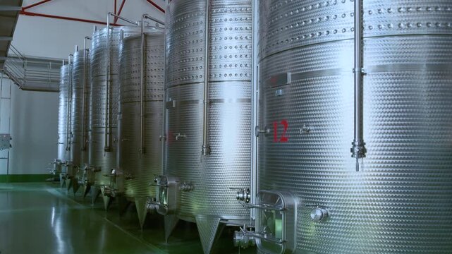 Row of large stainless steel fermentation and storage tanks in modern wine production factory. Industrial wine production in Armenia. Modern winery interior. Food and beverage technology