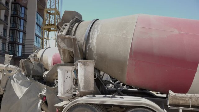 Concrete mixer truck drum slowly rotating at a construction site, preparing the cement for building a new residential block with a tower crane visible in the background on a sunny day