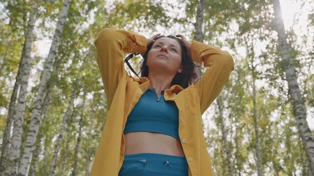 Fearless woman among lush trees. Confident woman boldly exploring lively green forest scene. Courageous female explorer standing confidently amidst energetic and lush woodland landscape